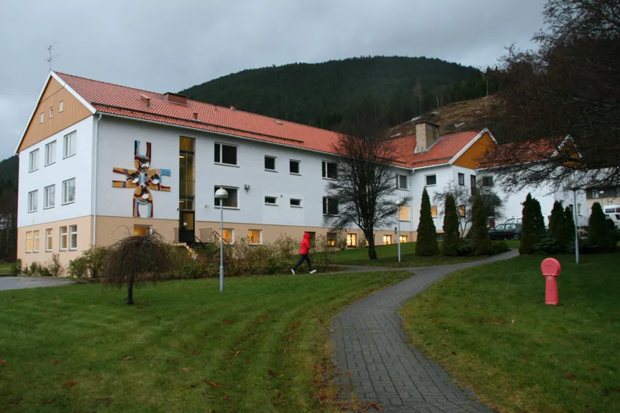 En person som går på en sti foran en bygning med rødt tak