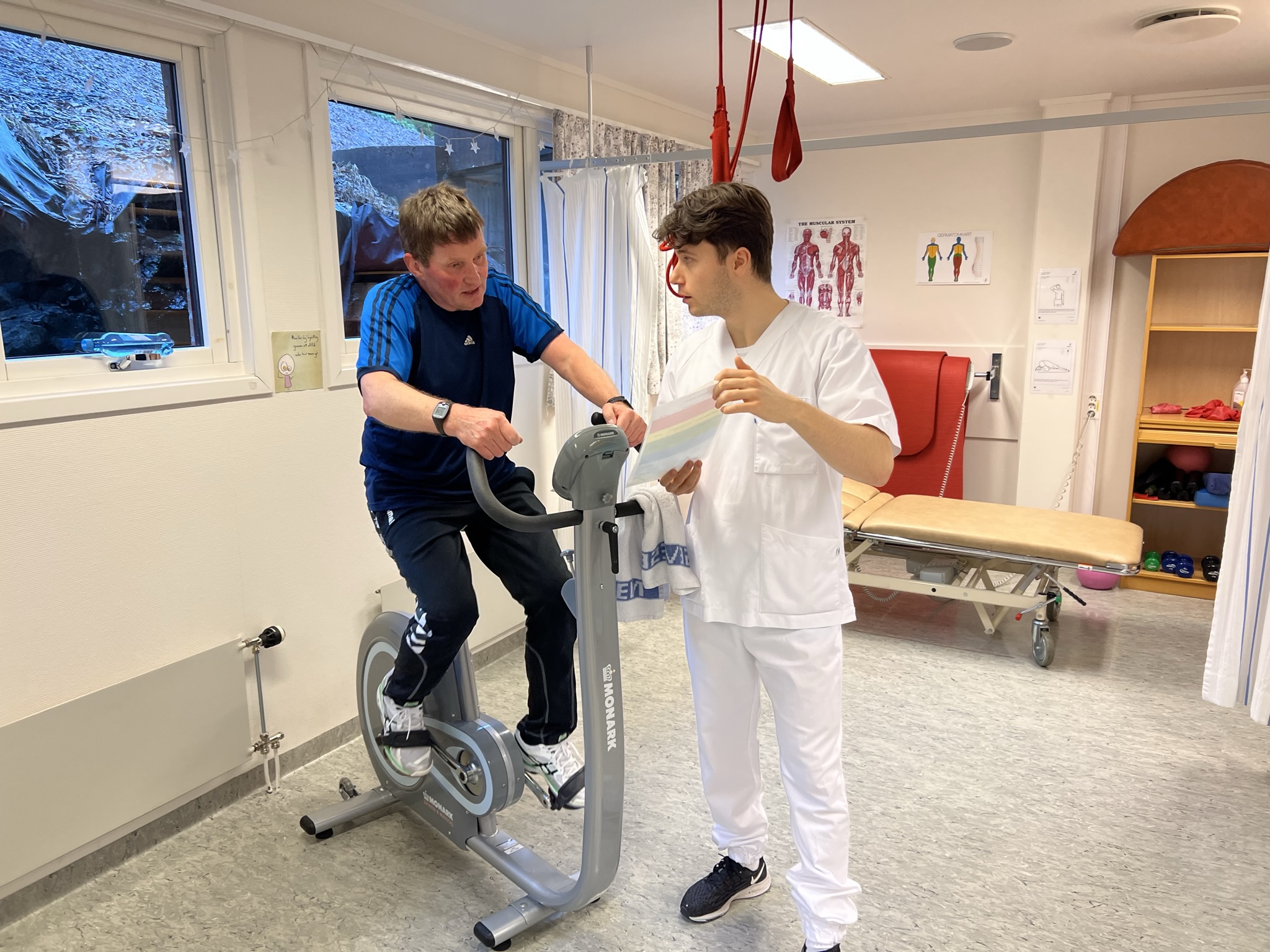 Ein pasient som syklar på ergometersykkel mens ein fysioterapeut føl med