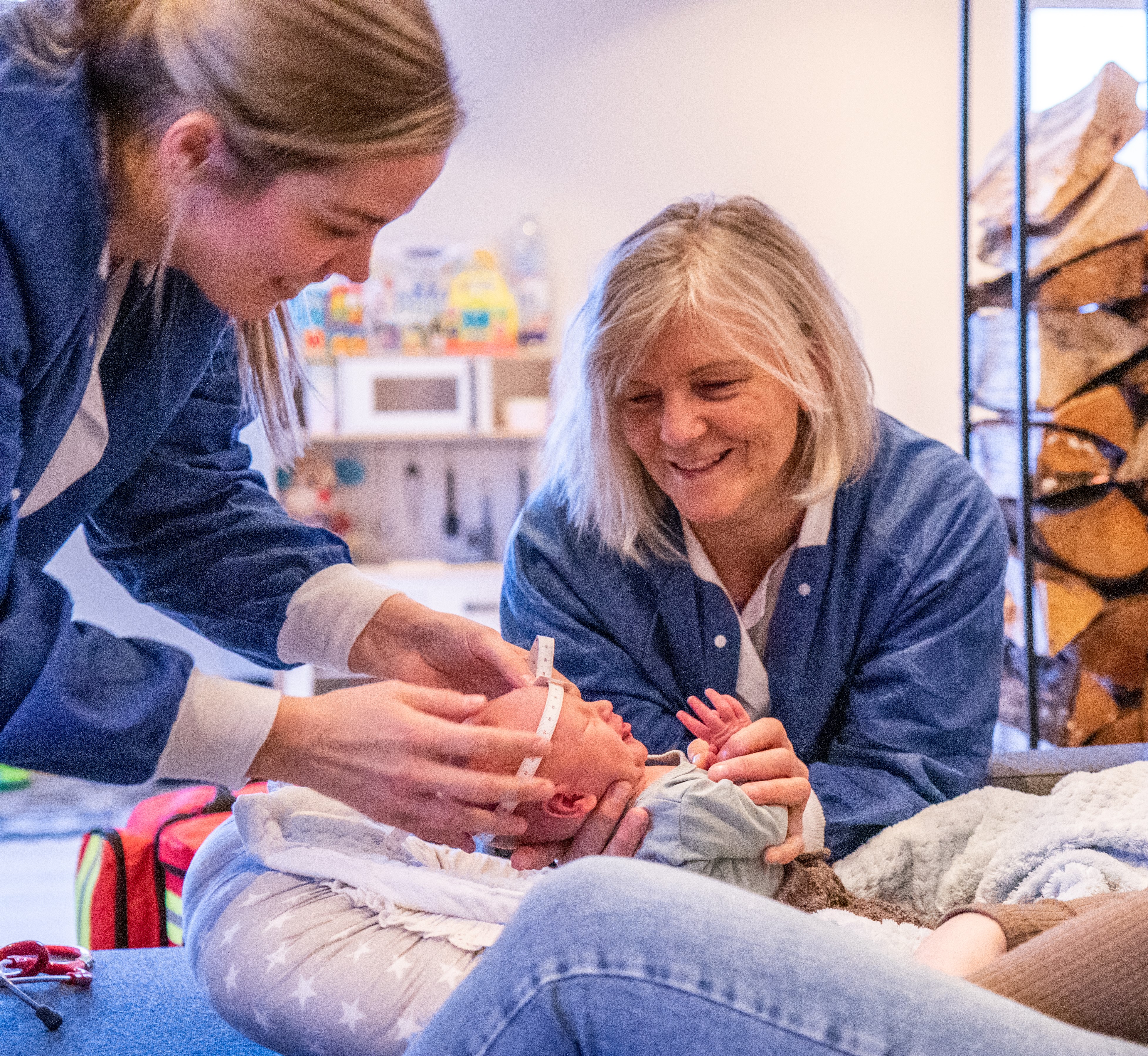 To kvinner i helseuniformer som måler omtrinsen på hodet til en nyfødt baby