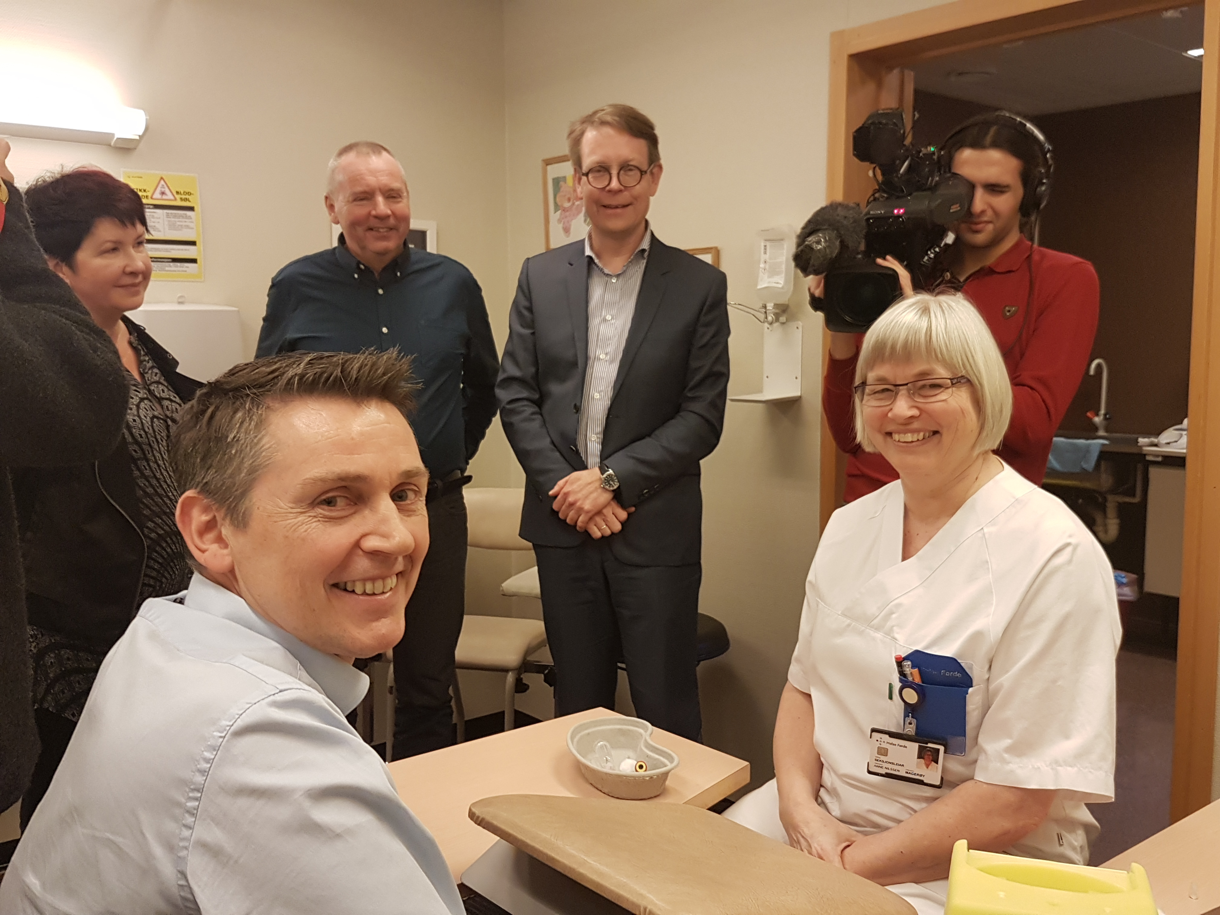 Ei rekke personar som står og sit rundt eit bord på sjukehuset