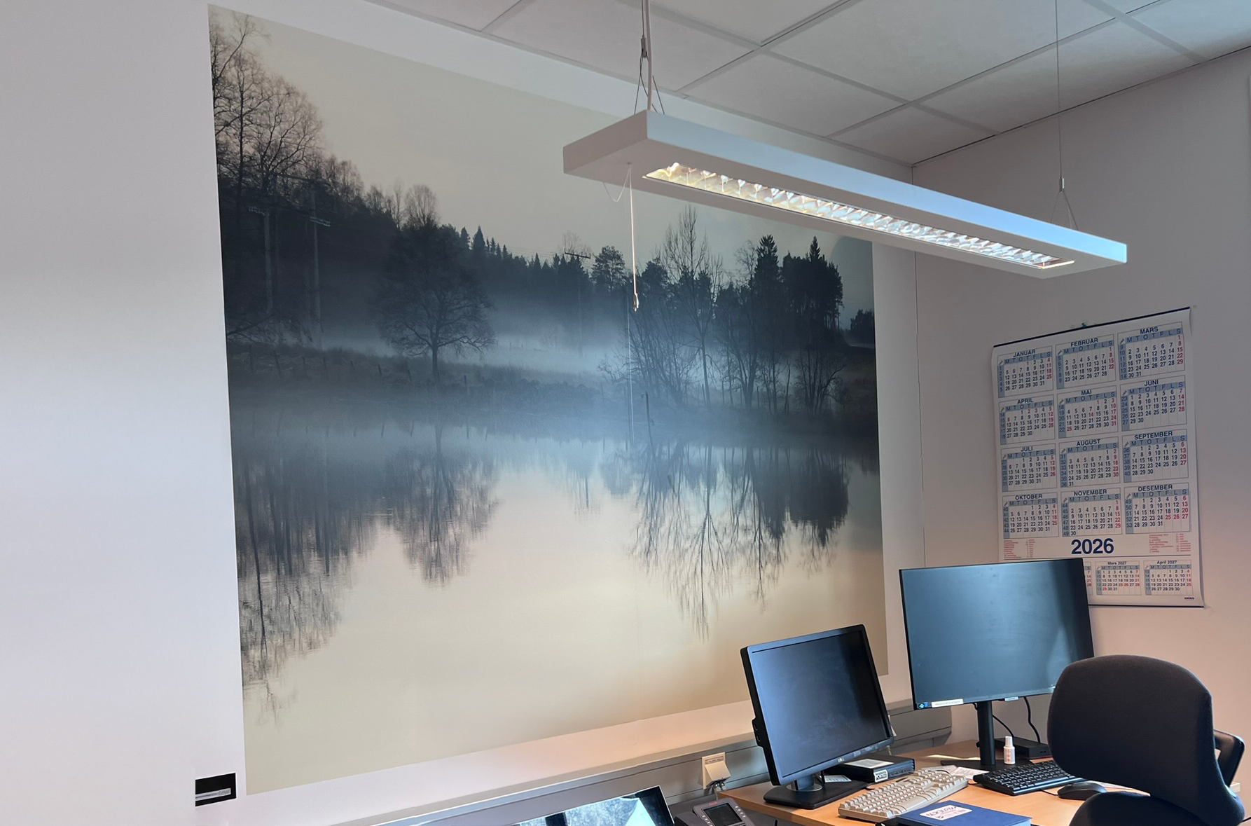 Fototapet på eit kontor som viser ein skoddekledd skumringstime ved vatnet