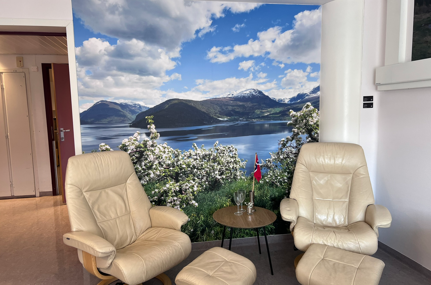 Eit barselrom med eit bord og to stolar, med ein fototapet i bakgrunnen som viser fruktblomstring