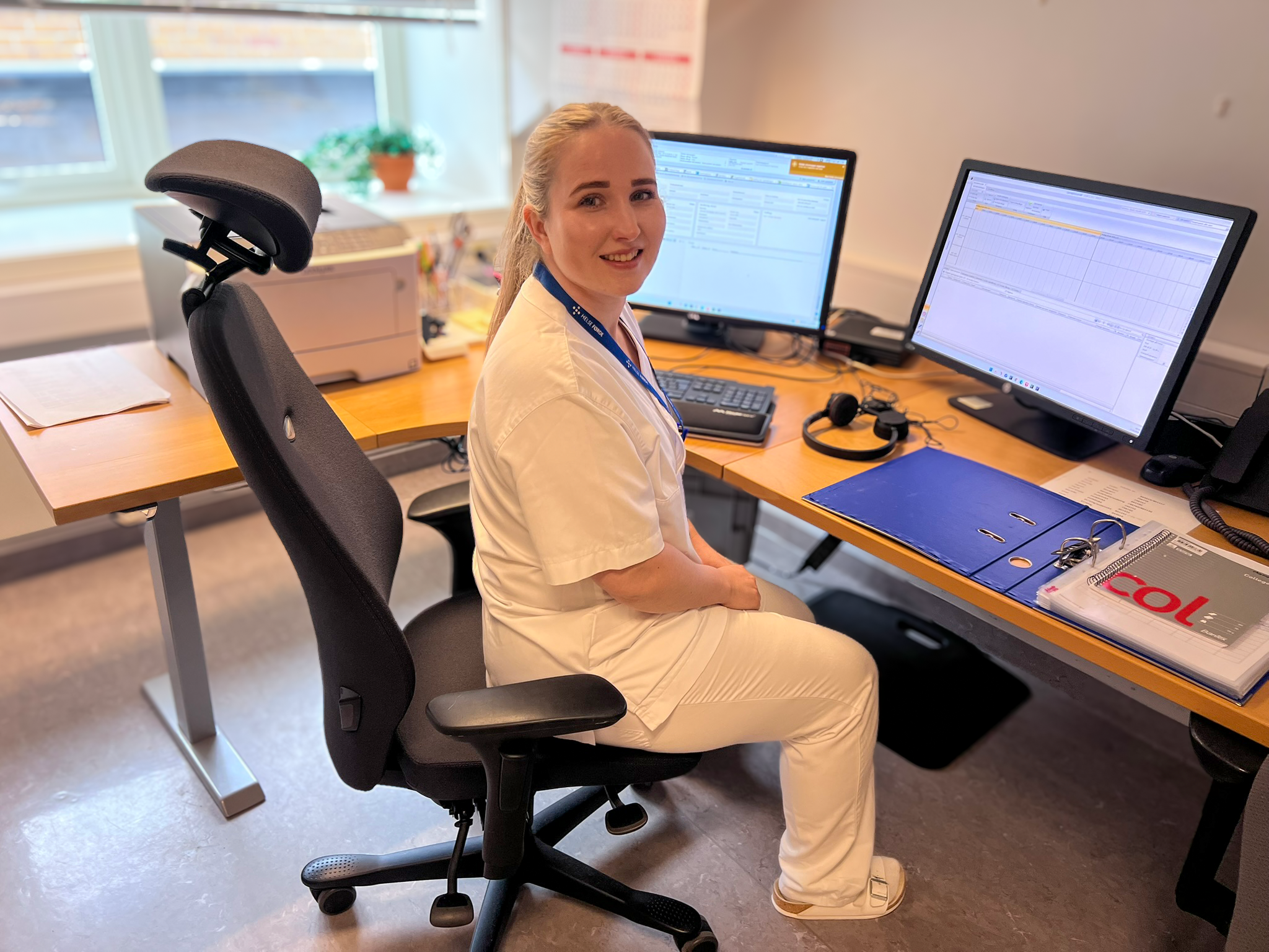 Ei kvinneleg helsesekretær som sit ved eit skrivebord med ei datamaskin framfor seg