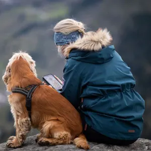 Ein person som sit utandørs på ein bergknaus saman med ein hund og ser på mobiltelefonen sin