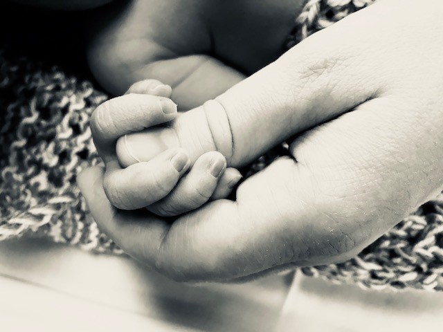 nyfødd babyhand som held i ei større hand
