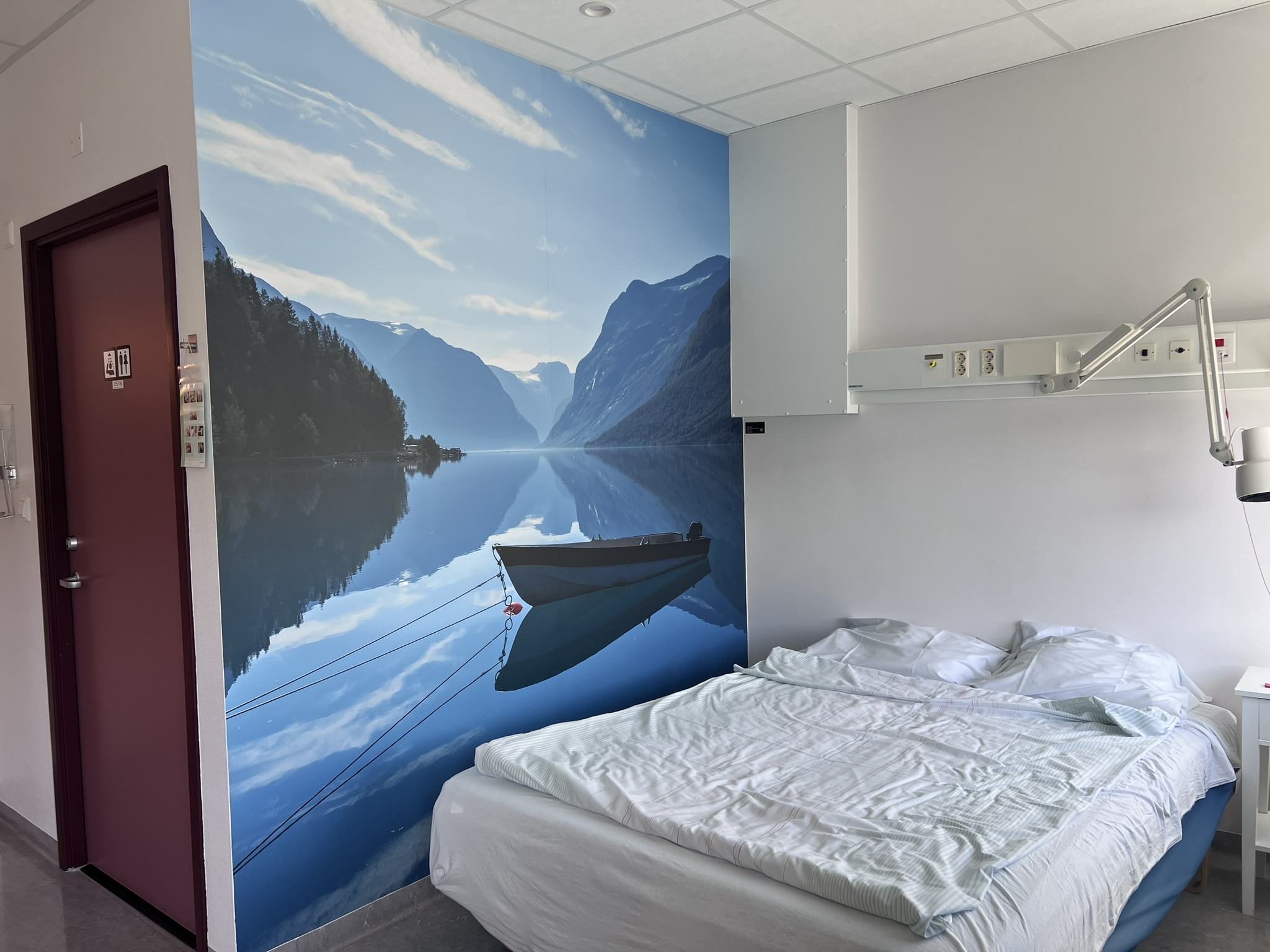 Eit pasientrom med fotokunst av ein båt som ligg på eit stille vatn.