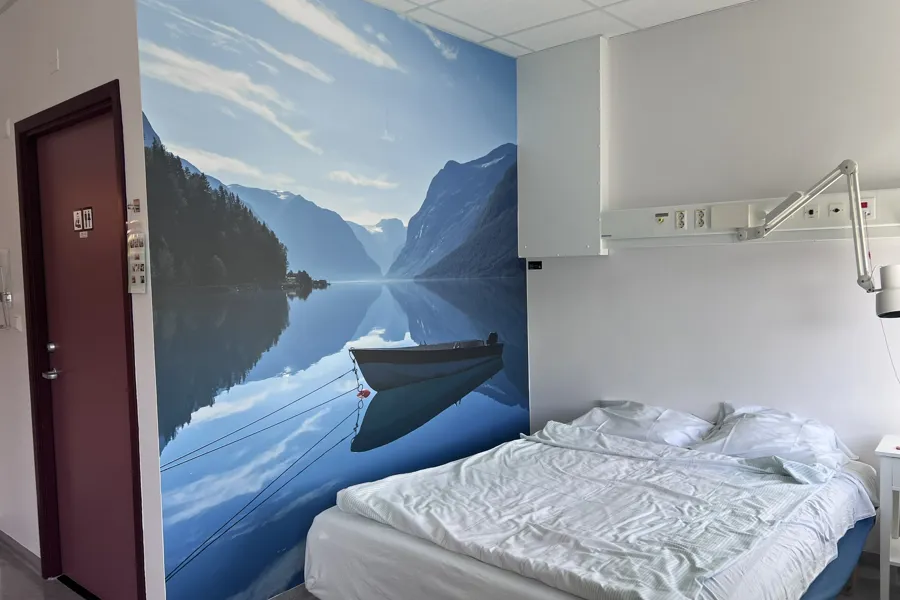 Eit pasientrom med fotokunst av ein båt som ligg på eit stille vatn.