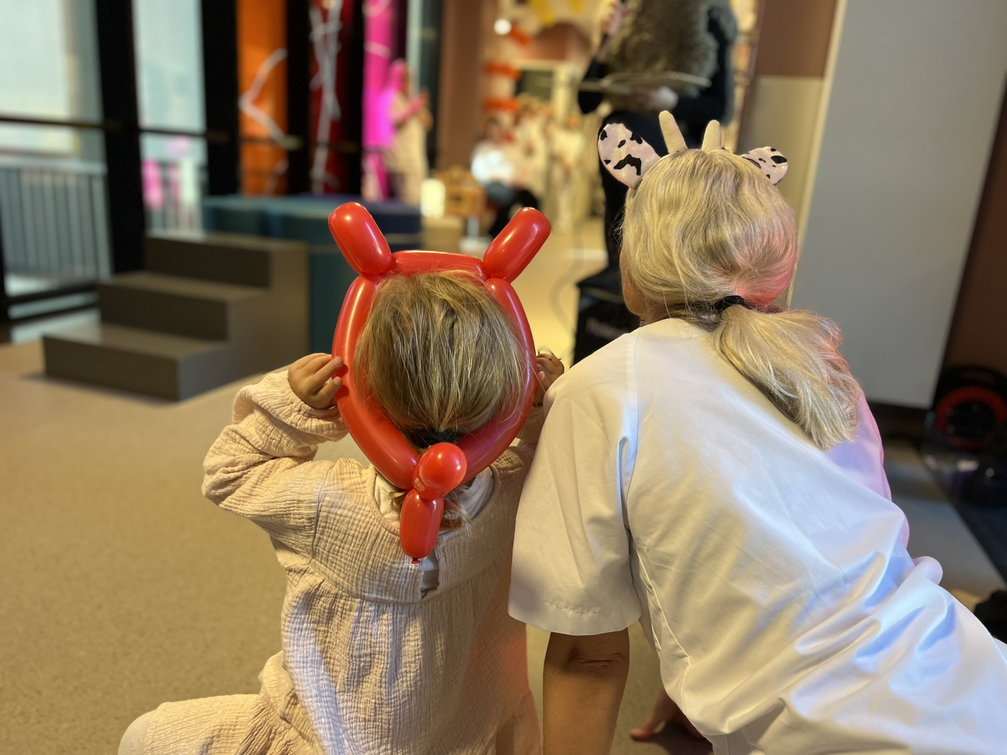 Et barn med ballonghorn på hodet, og en sykepleier som følger med på en eventyrfortelling