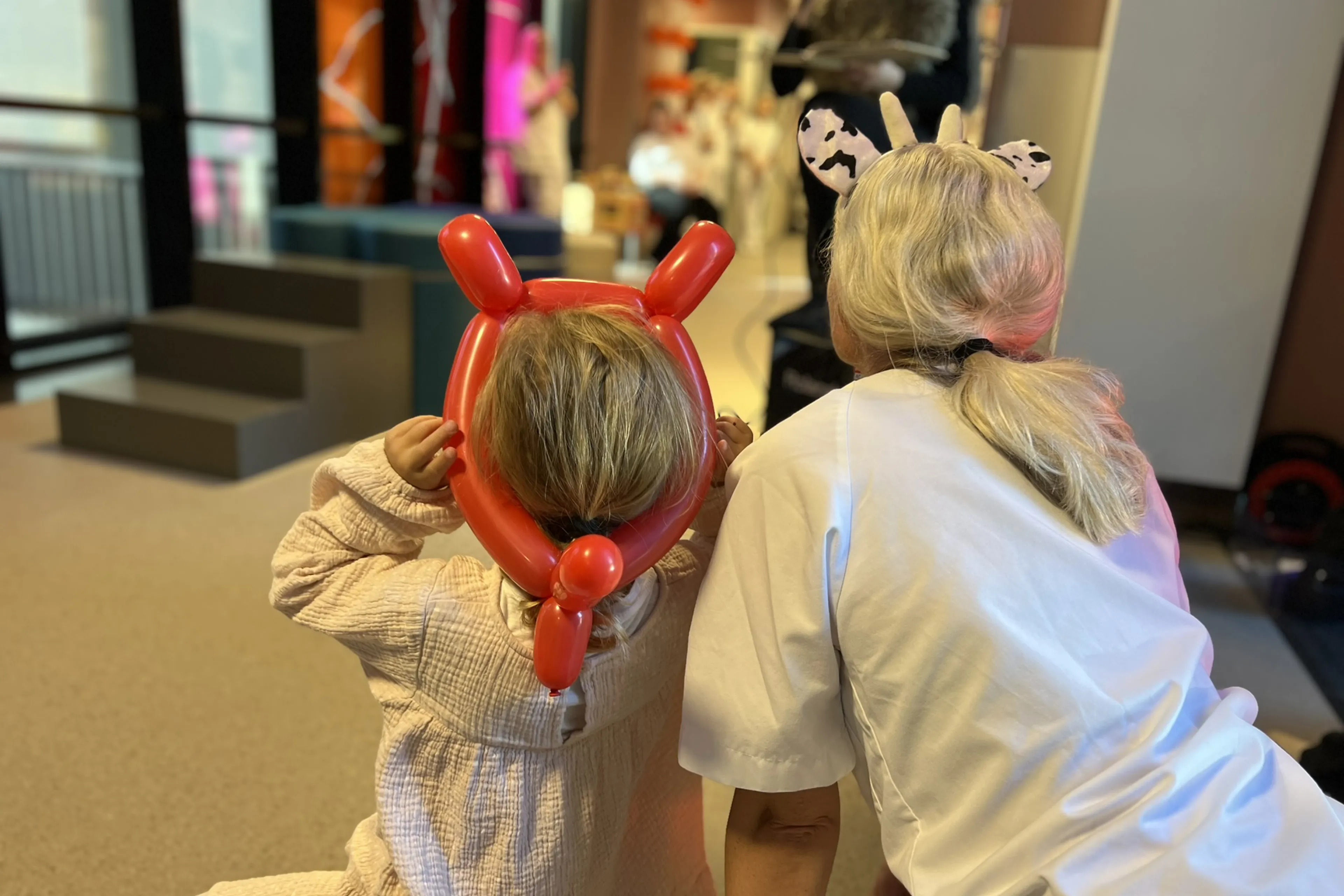 Et barn med ballonghorn på hodet, og en sykepleier som følger med på en eventyrfortelling