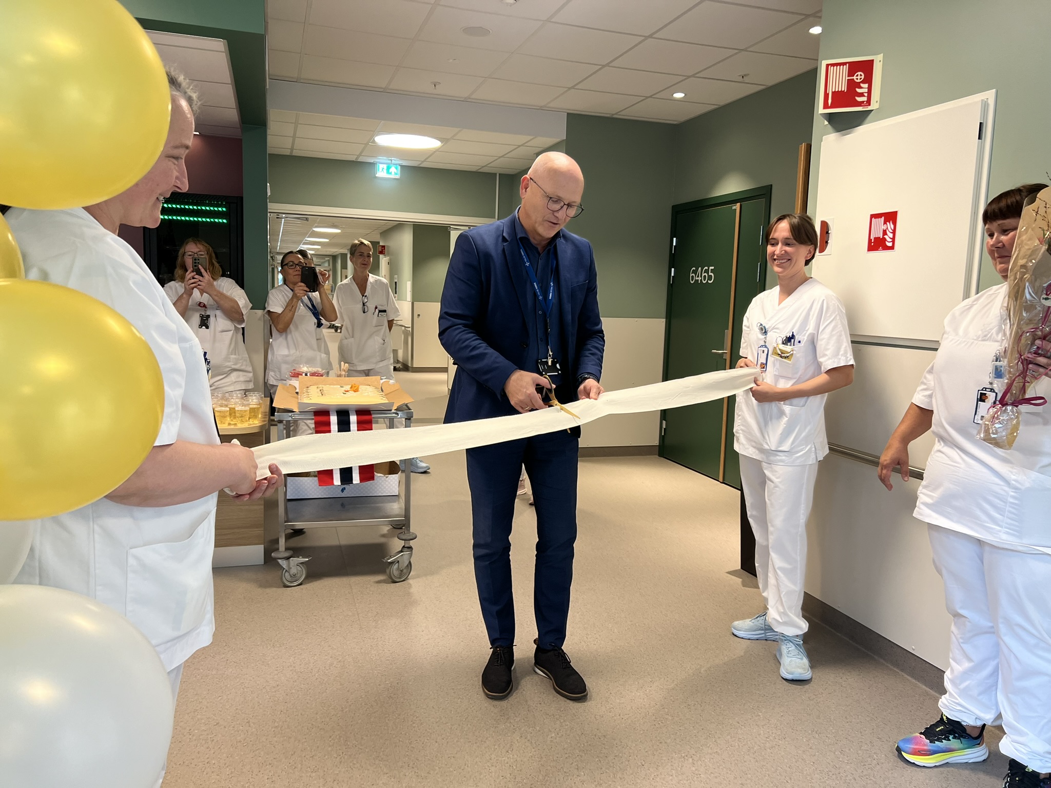 Administrerende direktør Arve Varden klipper bandasjesnoren, mens to sykepleiere holder snoren, under åpningen av kreft- og kirurgisk sengepost.