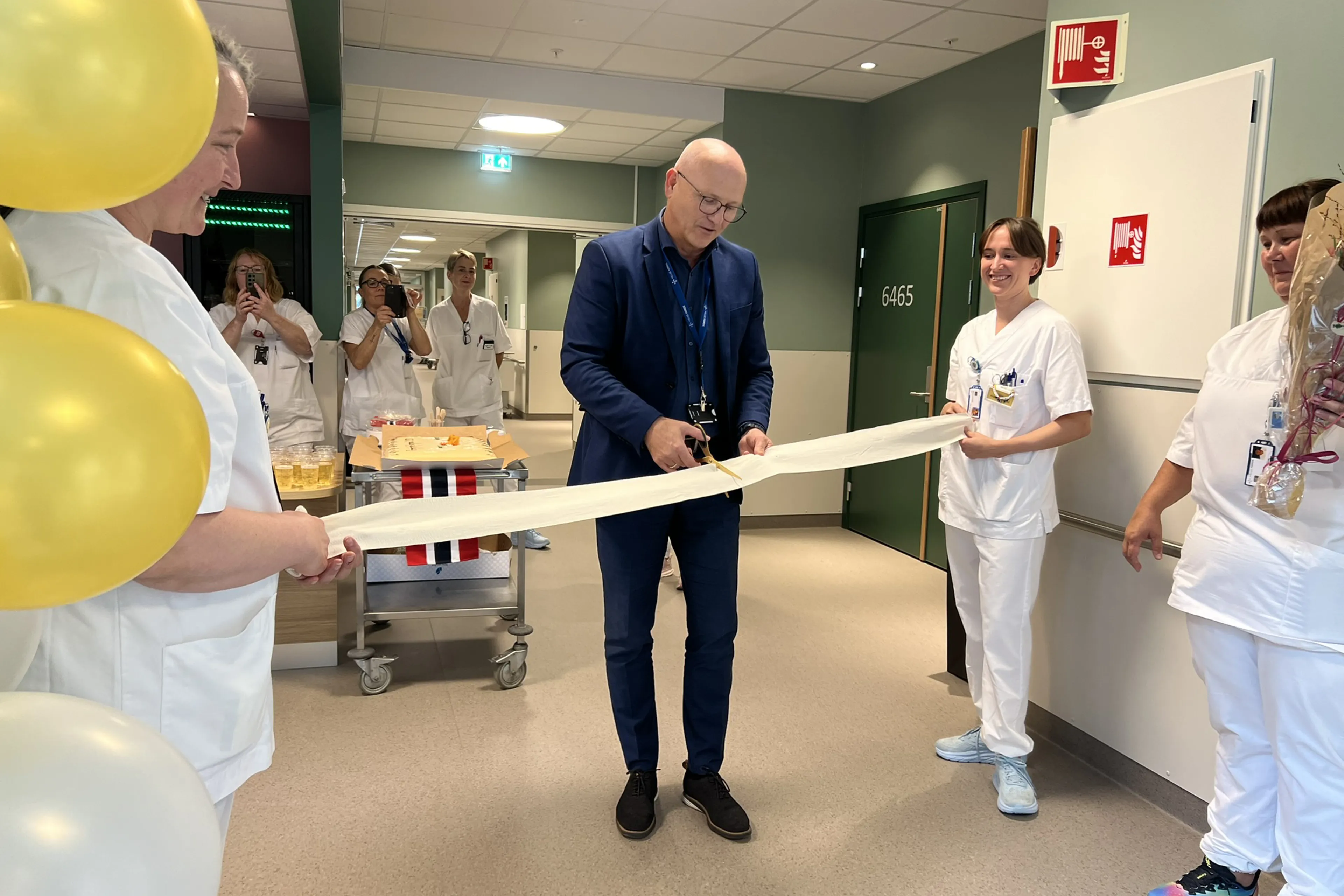 Administrerende direktør Arve Varden klipper bandasjesnoren, mens to sykepleiere holder snoren, under åpningen av kreft- og kirurgisk sengepost.