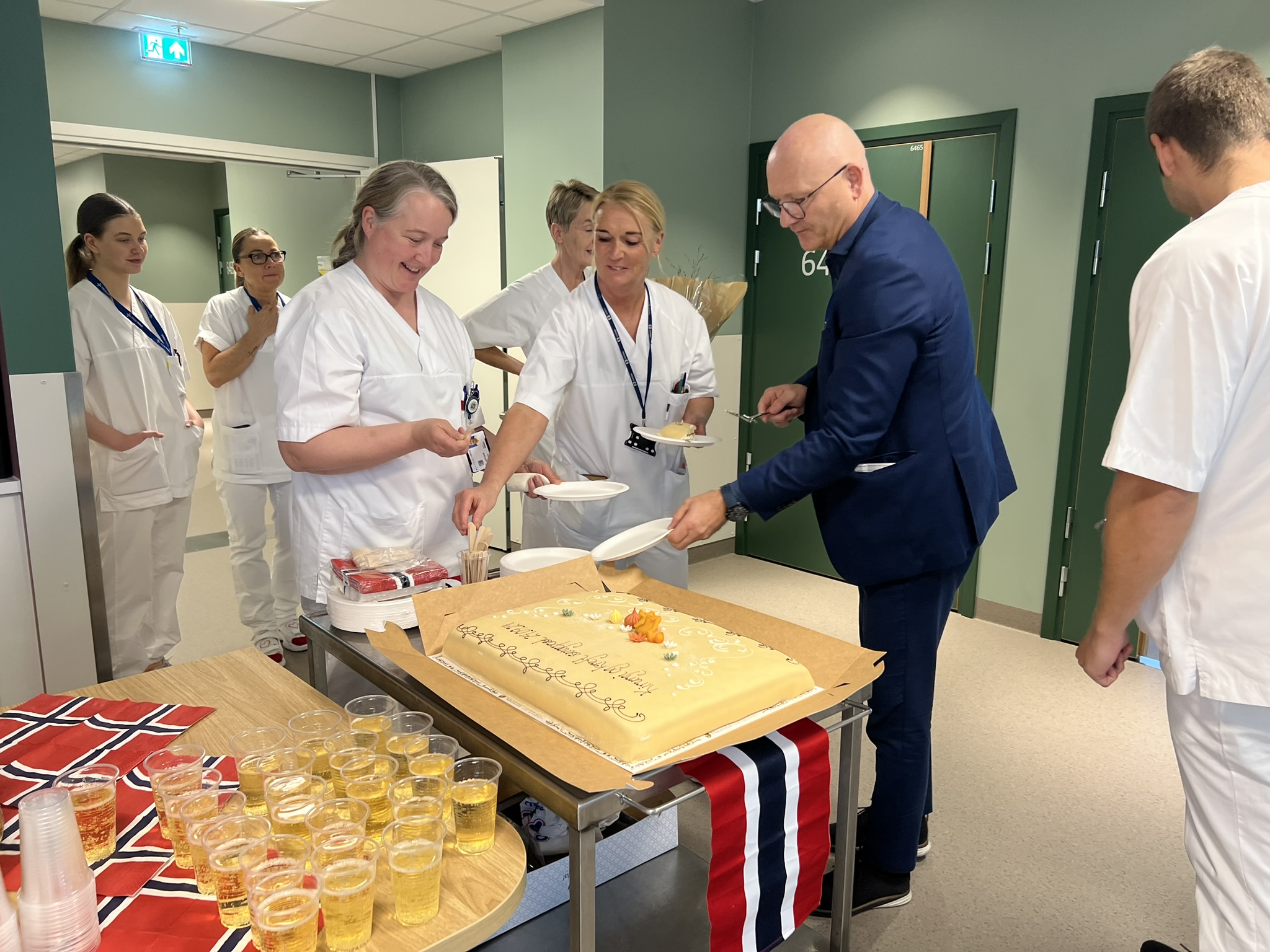 Ansatte i avdelingen, sammen med administrerende direktør, feirer flyttingen til Livabygget med kake, brus og norske flagg