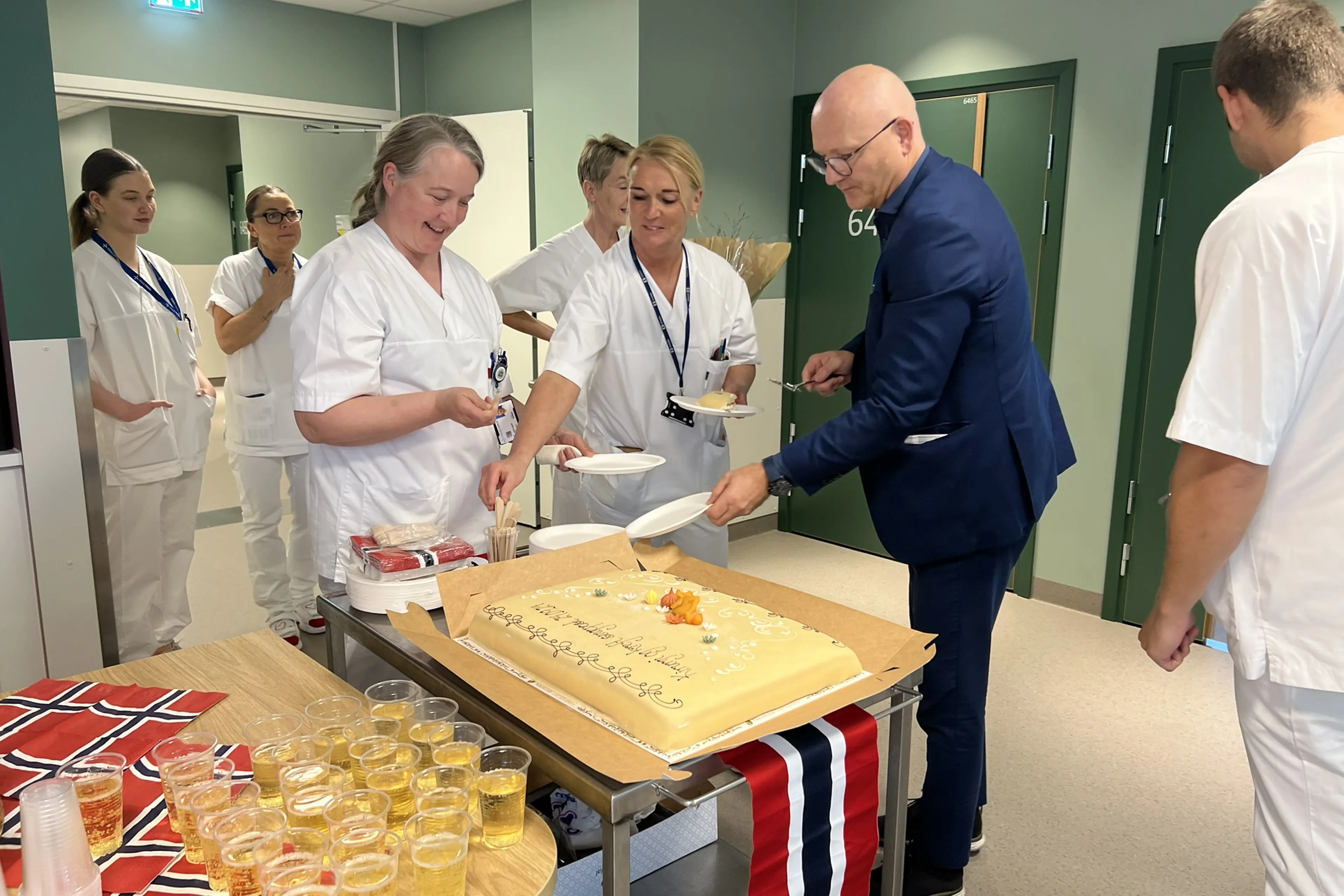 Ansatte i avdelingen, sammen med administrerende direktør, feirer flyttingen til Livabygget med kake, brus og norske flagg