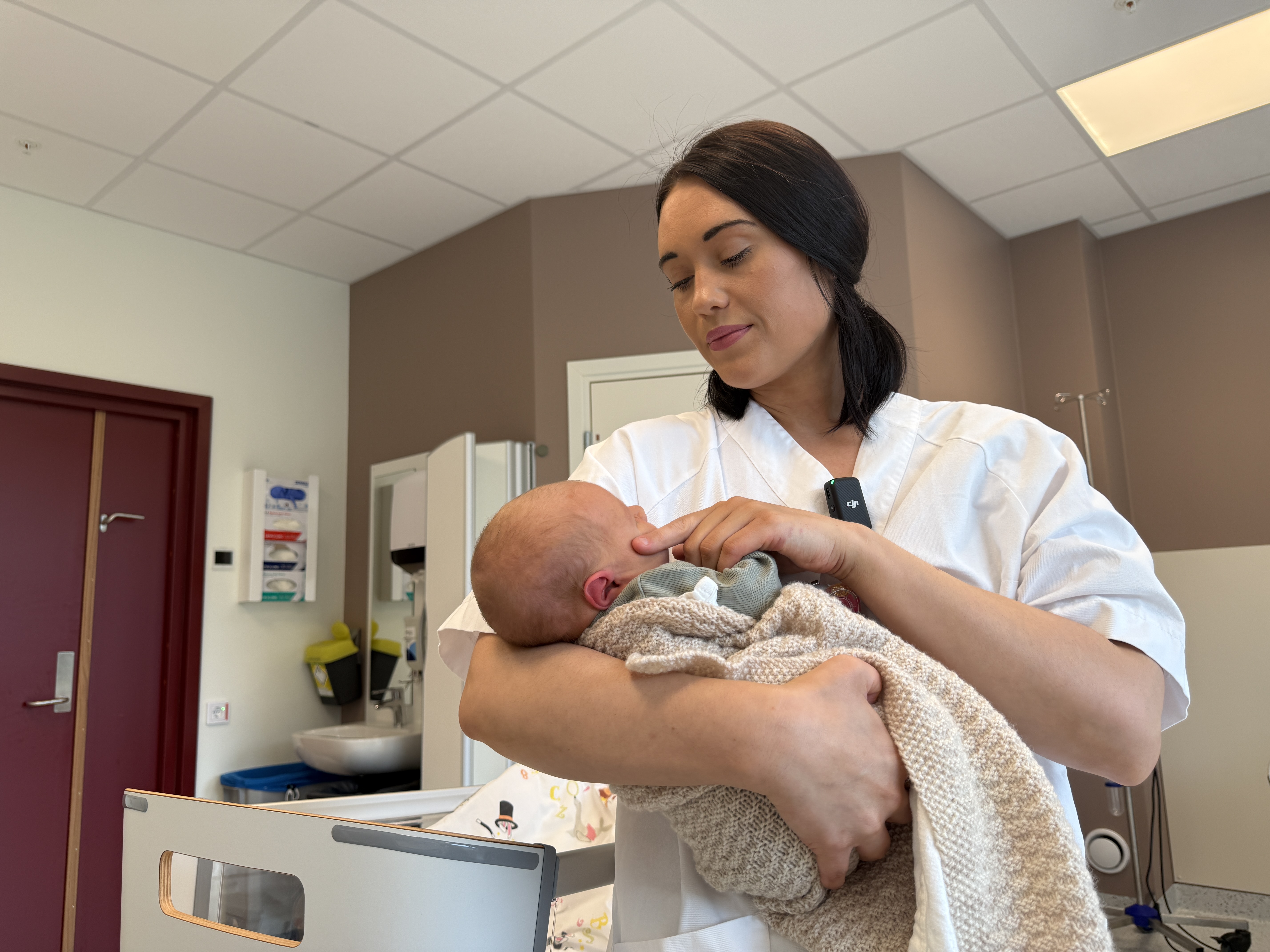 Ei ung kvinne i kvit uniform som held ein baby inne på ei fødestove