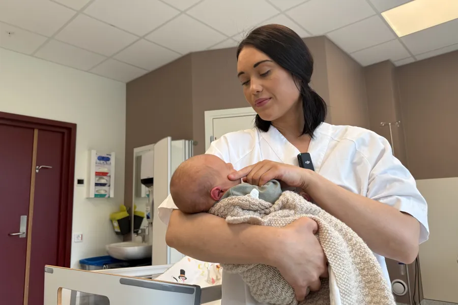 Ei ung kvinne i kvit uniform som held ein baby inne på ei fødestove