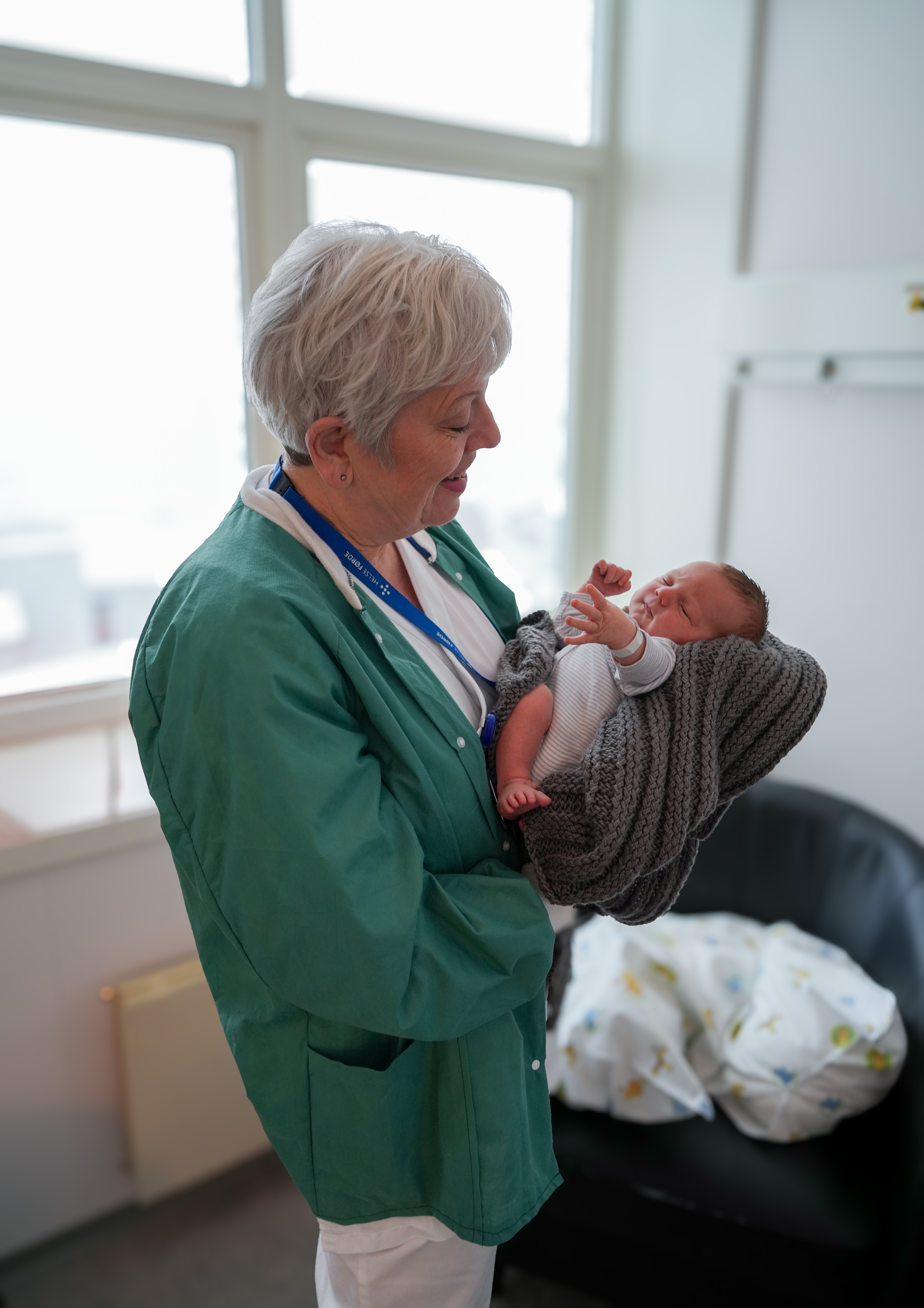 Ei jordmor som held ein nyfødt baby på inne på eit barselrom