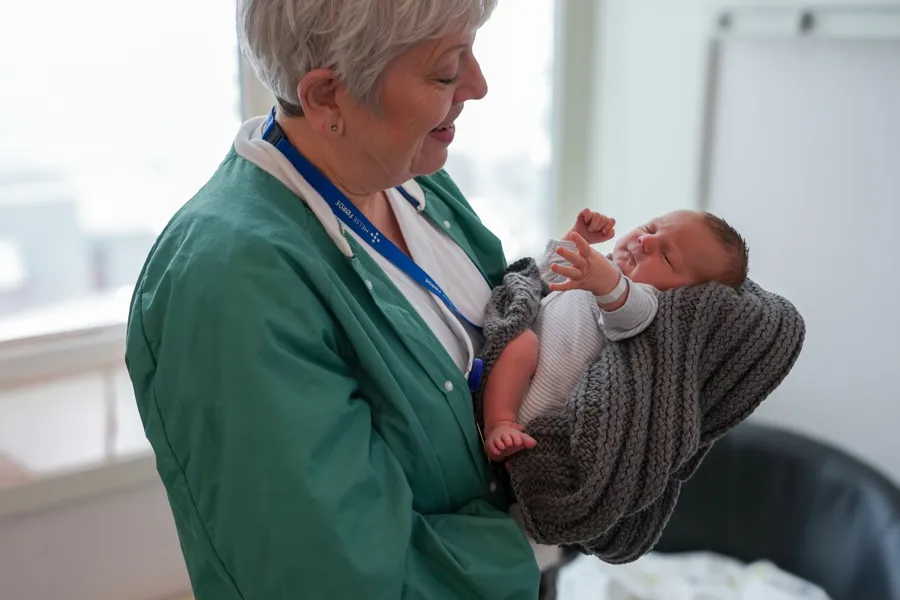 Ei jordmor som held ein nyfødt baby på inne på eit barselrom