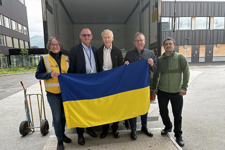 Representantar frå Førde Rotary klubb, Helse Førde og ein ukrainsk tolk held det Ukrainske flagget framfor lastebilen med operasjonsbordet som skal fraktast til Ukraina.