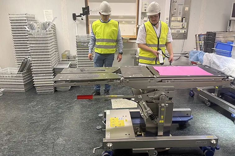 Eit par menn i sikkerheitsvestar som står ved sidan av eit operasjonsbord