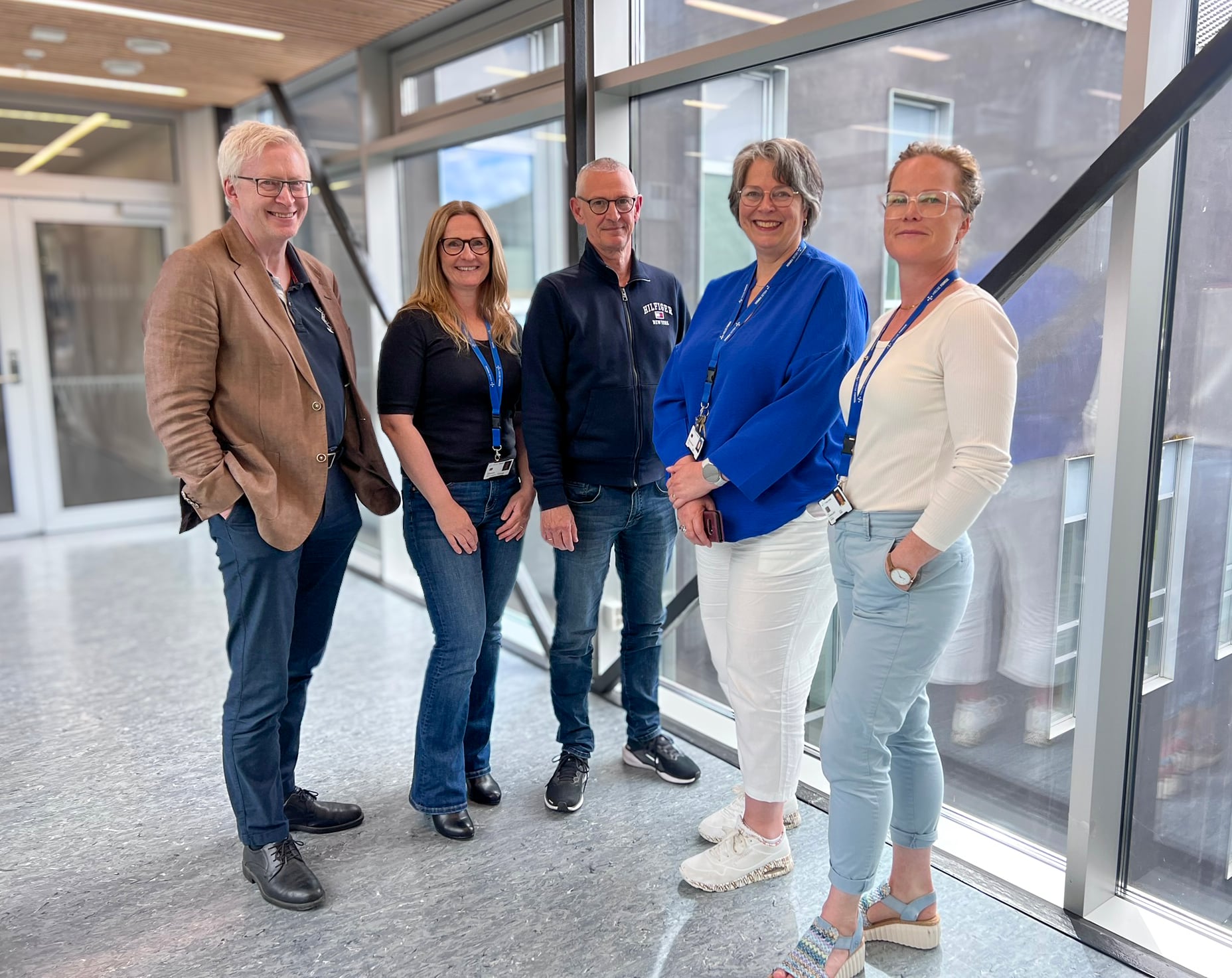 Fem personar som står i ein glasskorridor på sjukehuset.