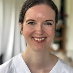 Portrett av ei kvinne i kvit uniform som smiler til kameraet
