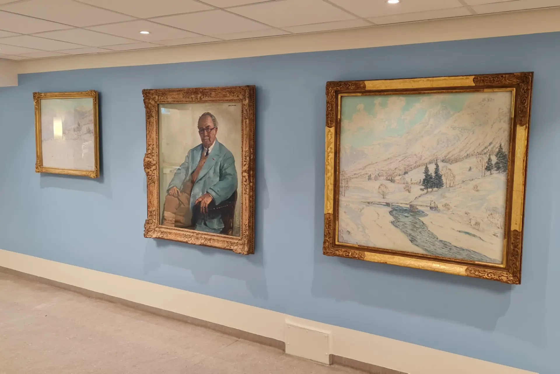 Tre måleri i gullrammer som heng på ein lyseblå vegg på sjukehuset