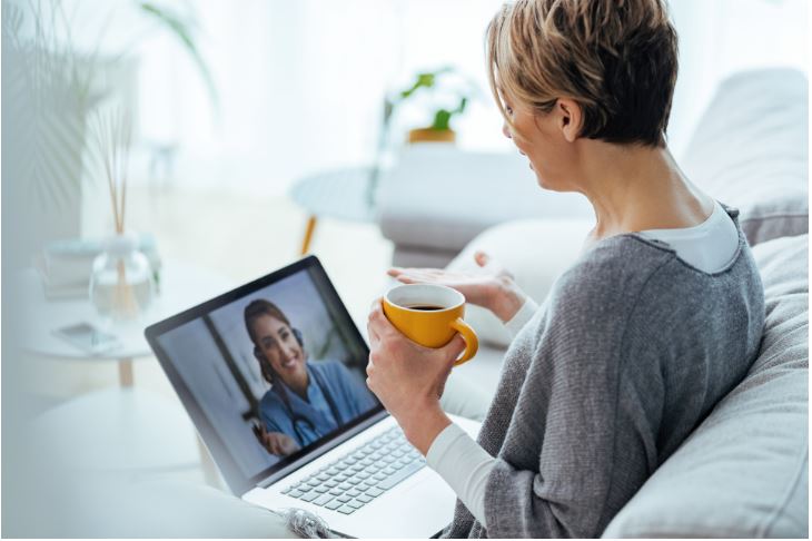 En kvinne som sitter i sofaen og har videokonferanse med helsepersonell