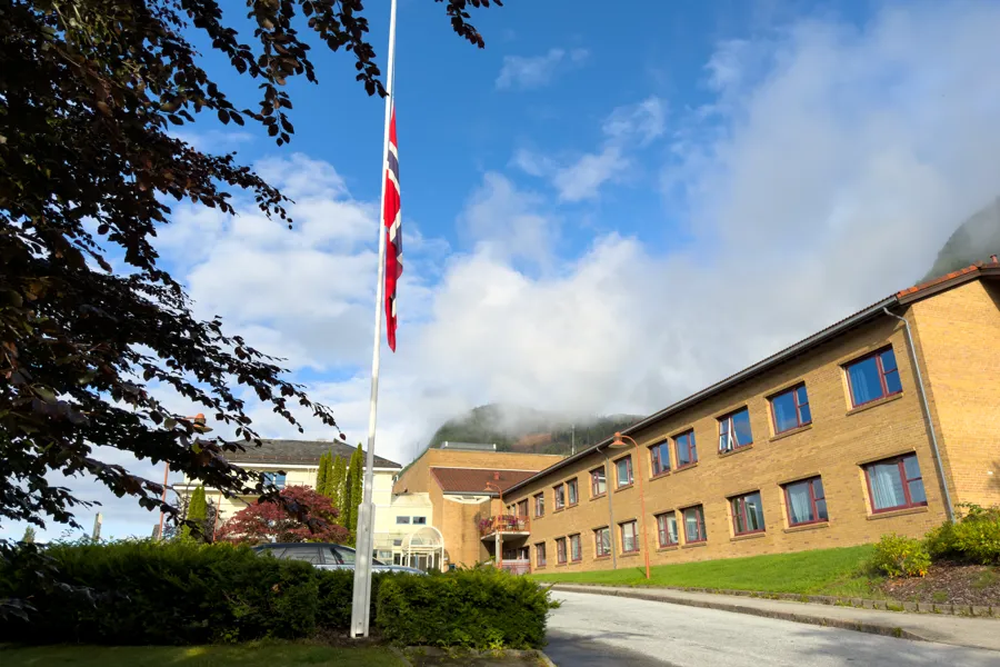Nordfjord sjukehus frå forsida med eit norsk flagg som vaiar på halv stang mot blå himmel
