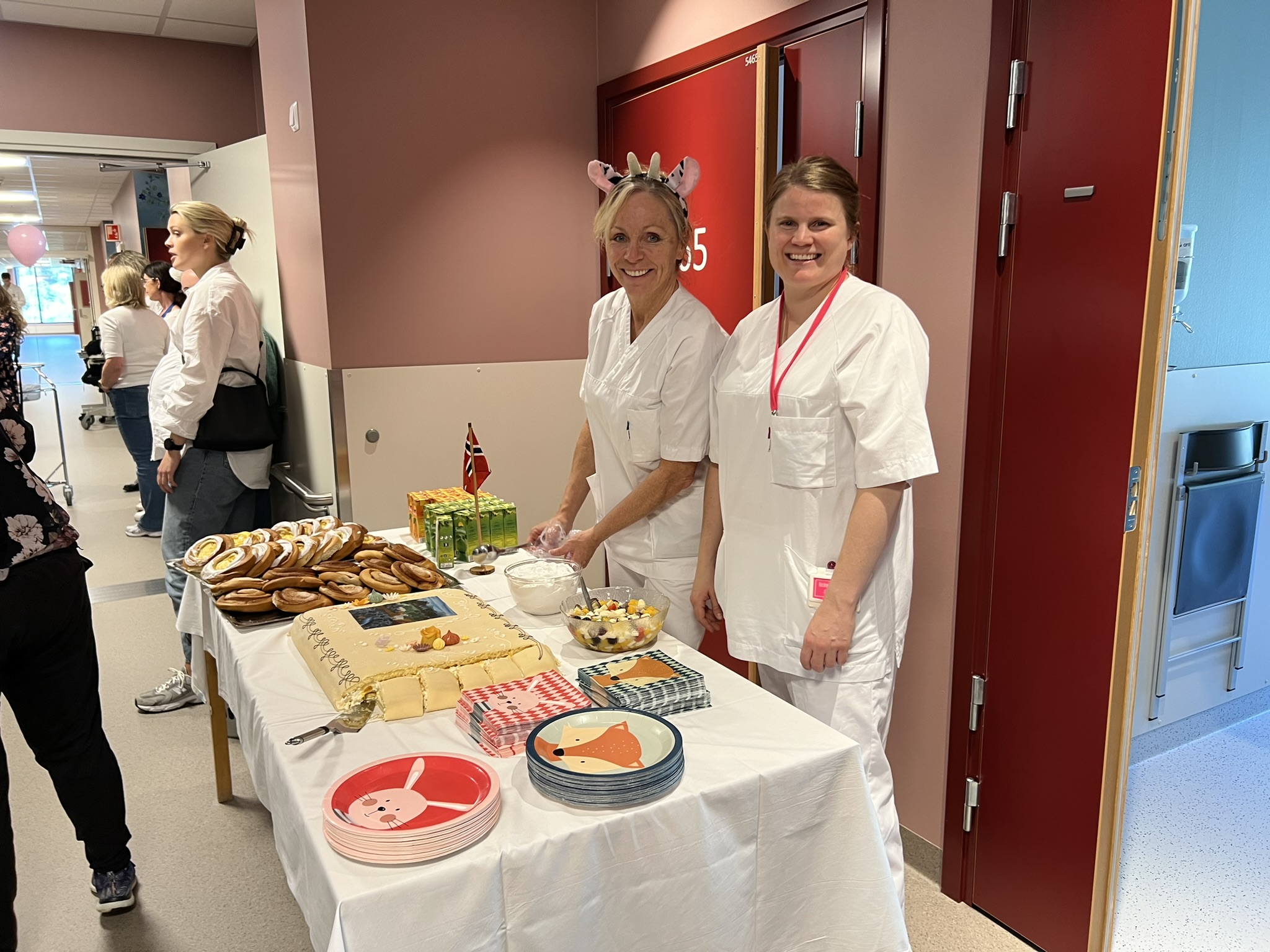 Et par kvinner i hvite forklær som står ved siden av et bord med mat på