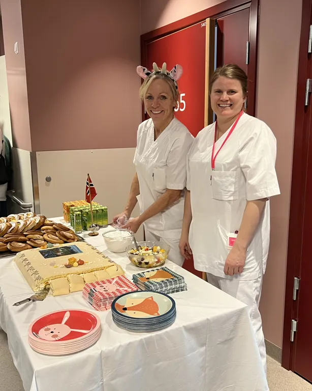 Et par kvinner i hvite forklær som står ved siden av et bord med mat på