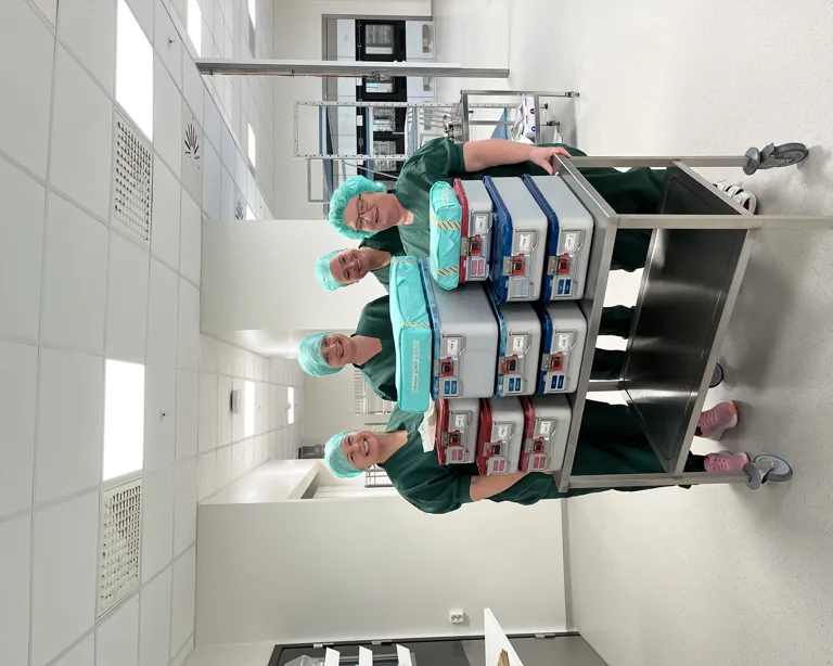 En gruppe kvinner i kirurgiske skrubb i et rom med en vogn full av medisinsk utstyr