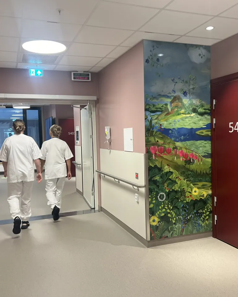 Eit par sjukepleiarar som går gjennom ein gang med eit stort maleri på veggen