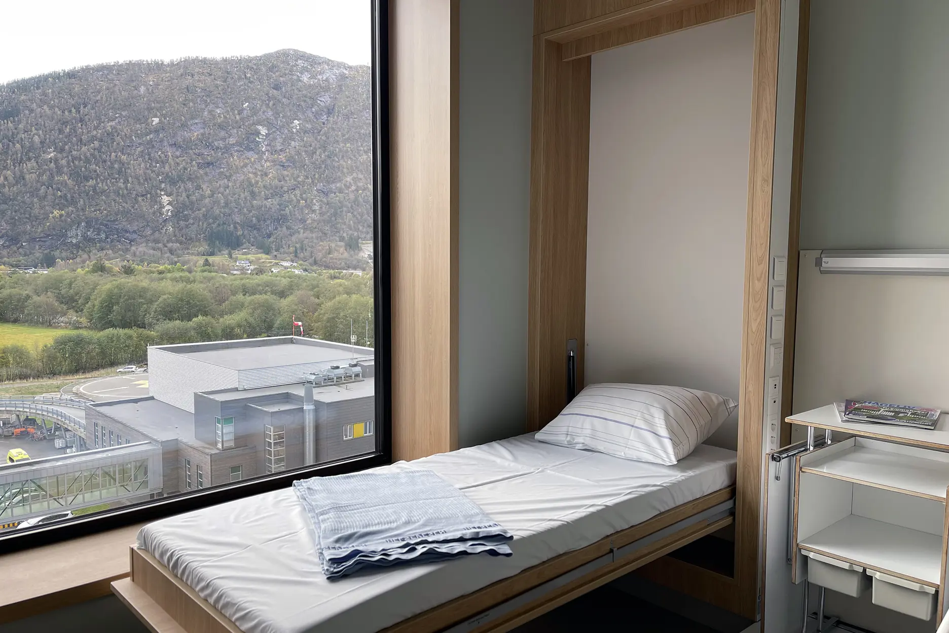 En seng med et hvitt laken og et vindu med utsikt over en by