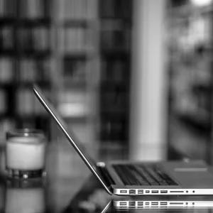 ein bærbar datamaskin og eit vassglas. I bakgrunnen ser vi bokhyller.