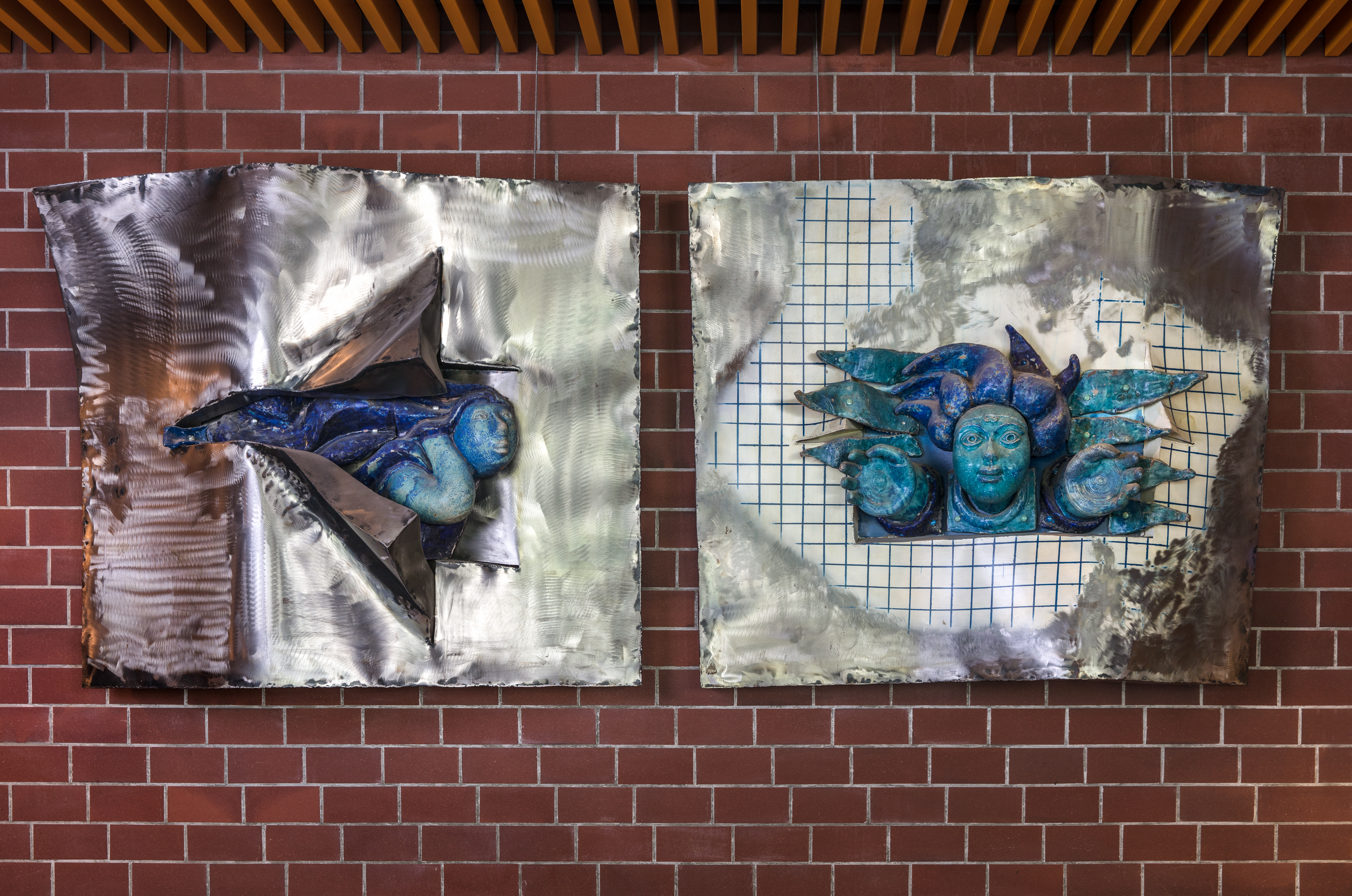 kunstverk i stål metall og keramikk som heng på ein mursteinsvegg