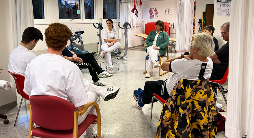 ei gruppe mennesker sit samla i ein ring inne i ein treningssal