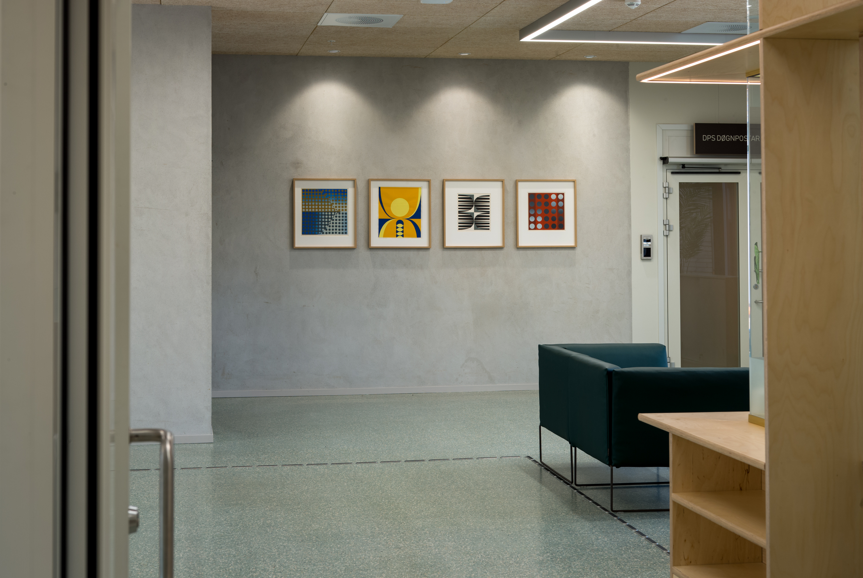 fire fargerike bilete i rammer som heng på ein grå vegg med ein grøn stol framfor