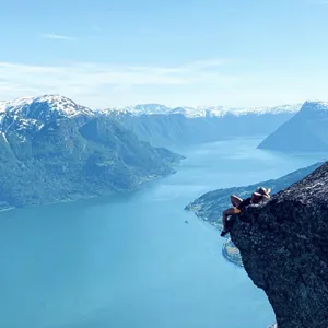 ein person ligg på ein fjellknaus og ser utover fjorden og fjella rundt