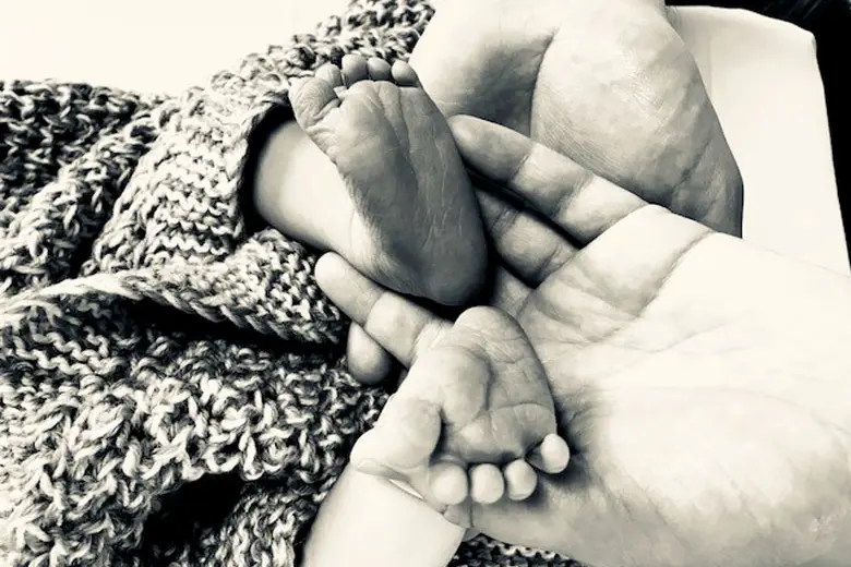 babyføter som stikk ut frå eit teppe i handa på ein person