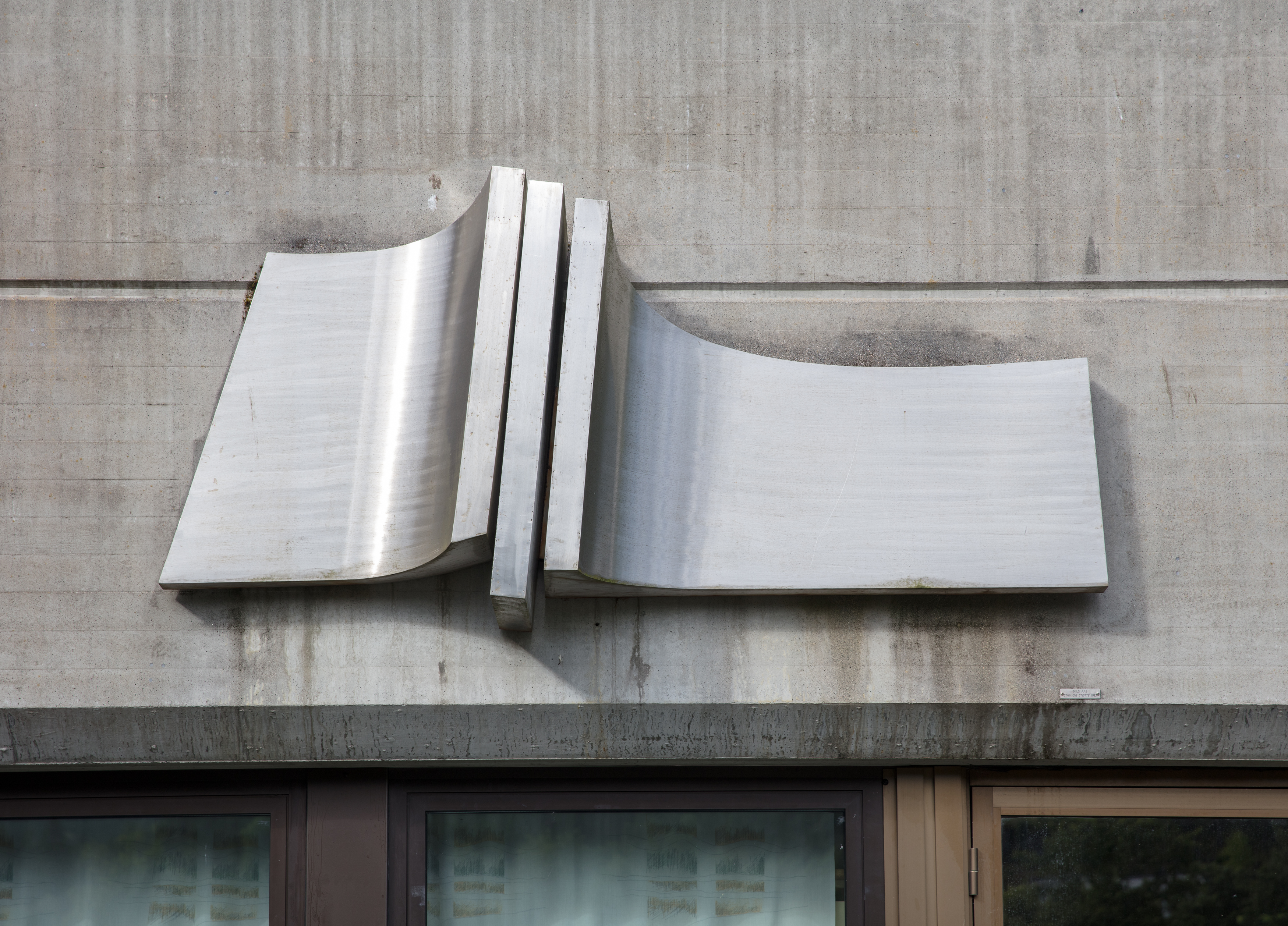 komposisjon i stål som er samansett av tre ståleiningar som heng på ein betongvegg utandørs