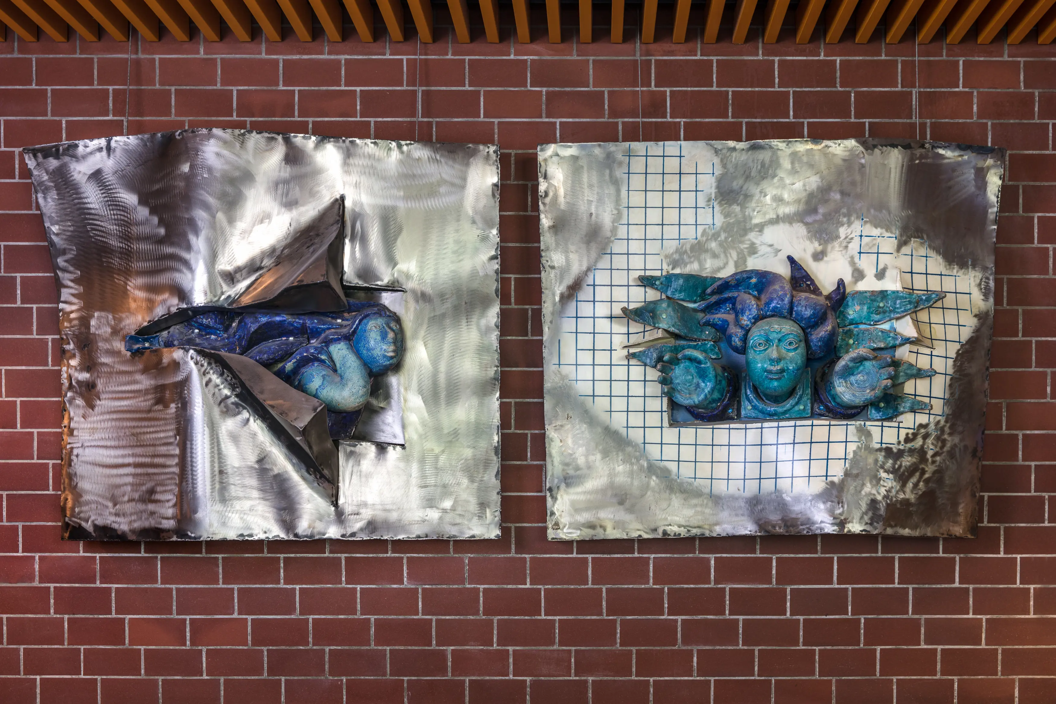 kunstverk av keramikk og stål som forstiller personar som bryt seg gjennom stålet. Heng på ein raud mursteinsvegg.