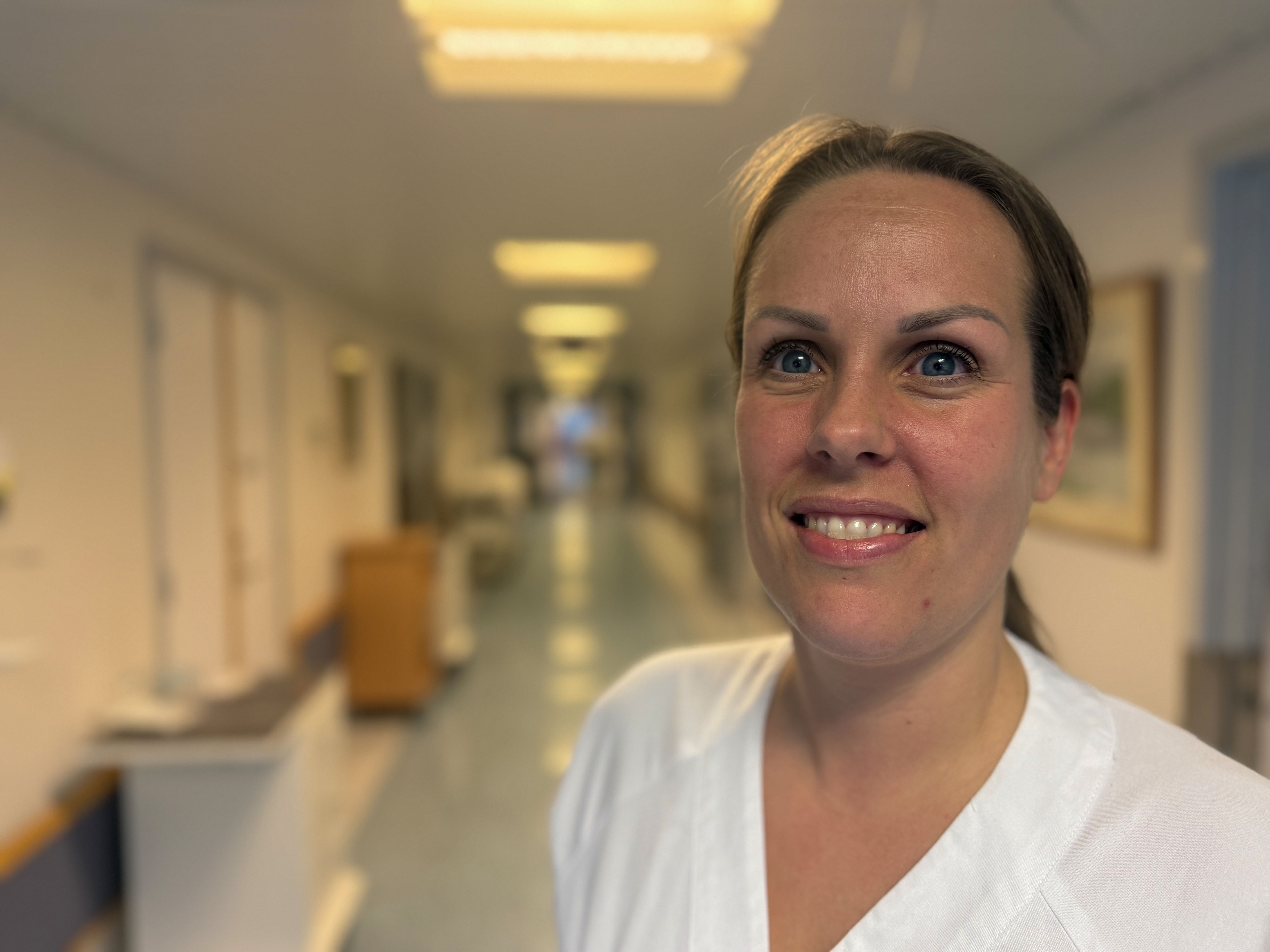 Ei ung og smilande kvinne i kvit uniform i ein sjukehuskorridor