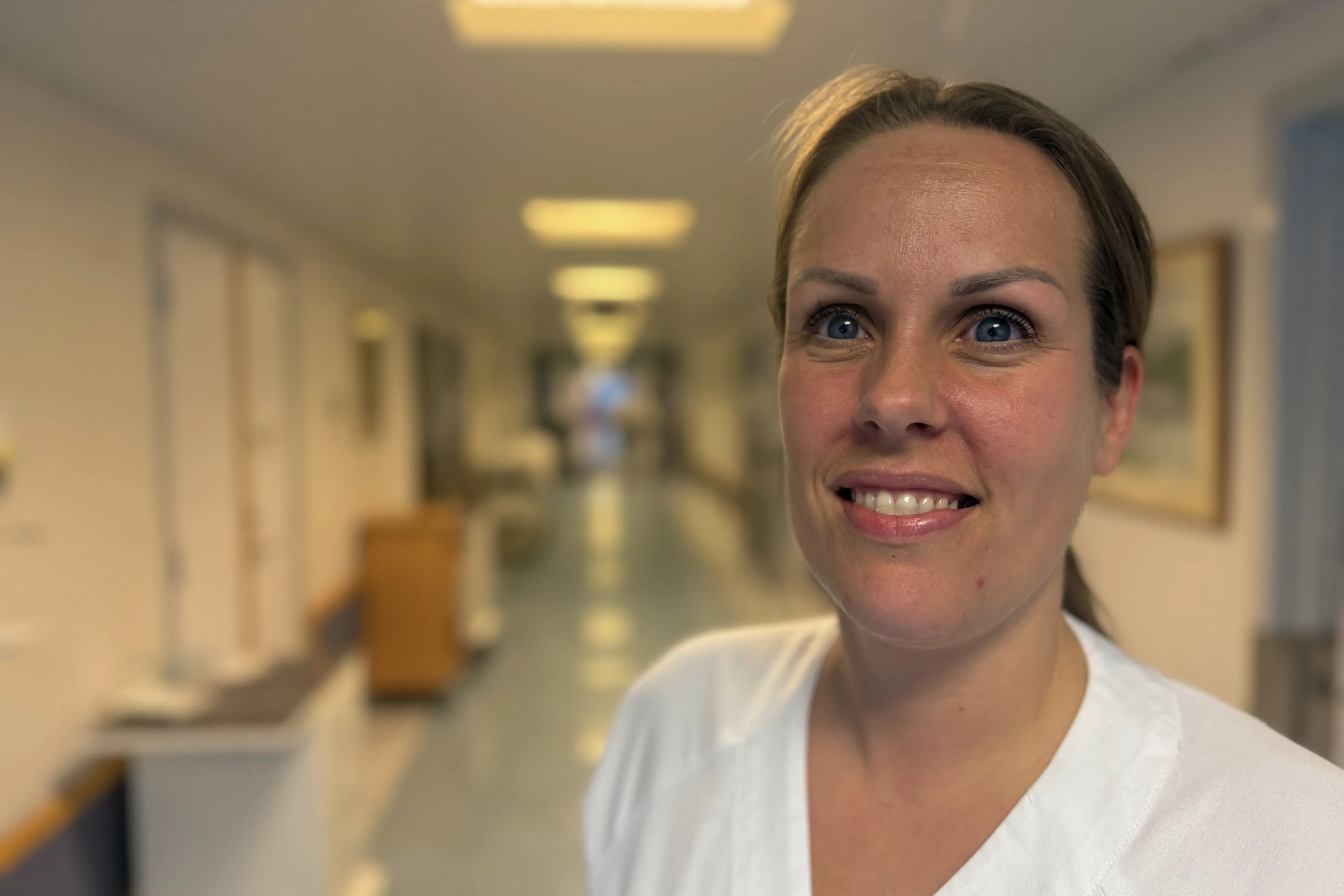 Ei ung og smilande kvinne i kvit uniform i ein sjukehuskorridor