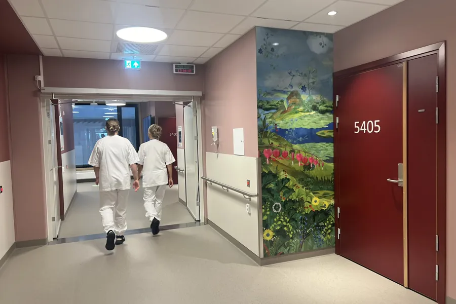 Et par uniformkledde går gjennom en gang med et stort maleri på veggen