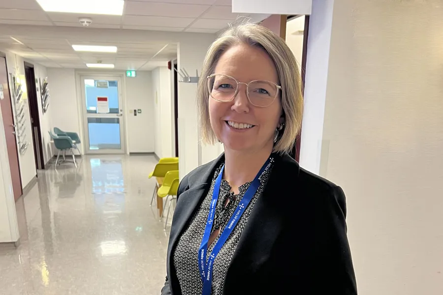 Ei kvinne med briller som står i ein sjukehuskorridor