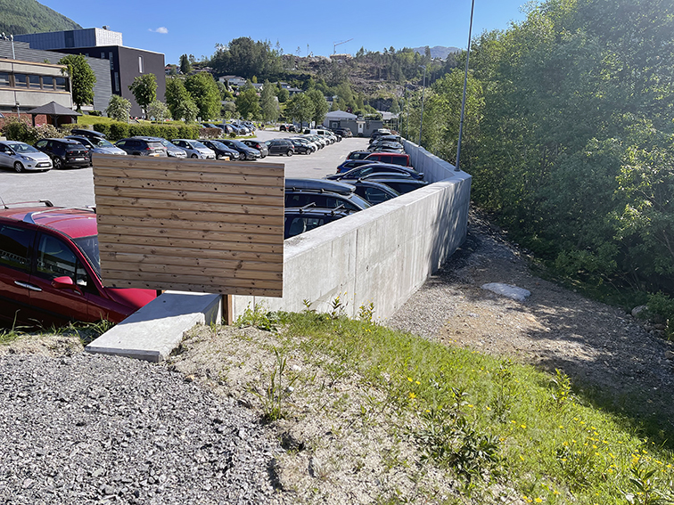 Ein parkeringsplass med bilar og ein betongmur